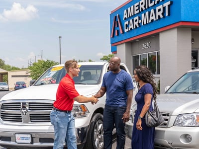 A Car-Mart Associate greeting a customer and his wife while standing near the couple's trade-in and new truck.