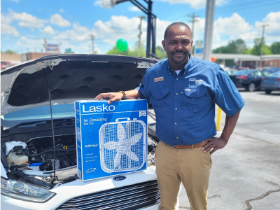 Car-Mart General Manager, Dishawn Bell, holding a box fan on the open hood of a car